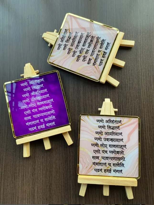 Acrylic Navakar Mantra frame (4 x 4.5 inch) with golden border, wooden stand, and available in two colours – Purple and White. Ideal for home or office decor.